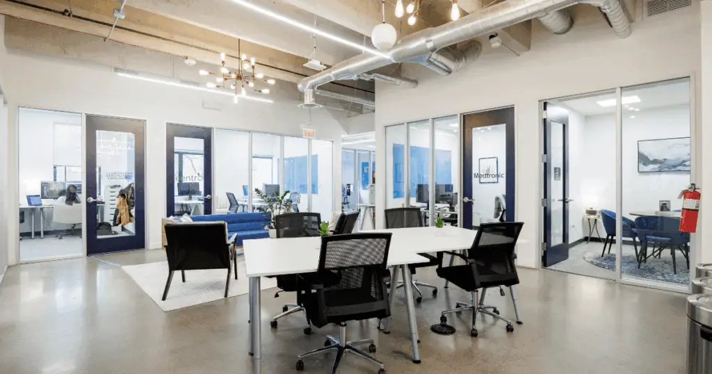 Open hot desk workspace at Strive Coworking Workspaces with shared tables, ergonomic seating, and glass-walled private offices.
