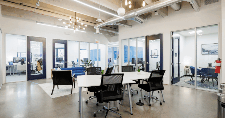 Open hot desk workspace at Strive Coworking Workspaces with shared tables, ergonomic seating, and glass-walled private offices.