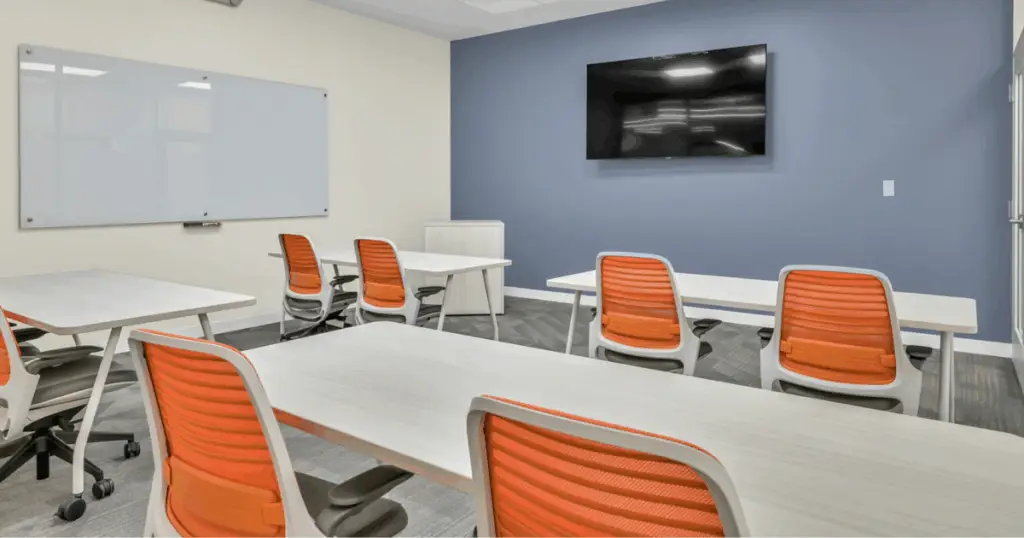 Conference room with desks, whiteboard, and TV screen at Strive Coworking Workspaces in Cypress, Texas