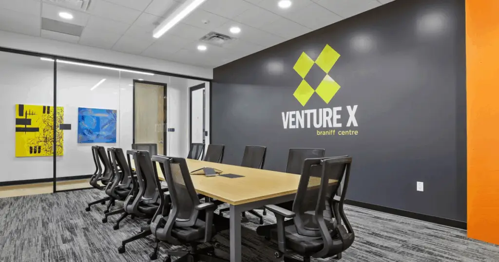 Conference room inside Venture X Braniff Centre coworking space in Dallas, Texas, featuring a modern meeting table, ergonomic chairs, and branded wall signage.