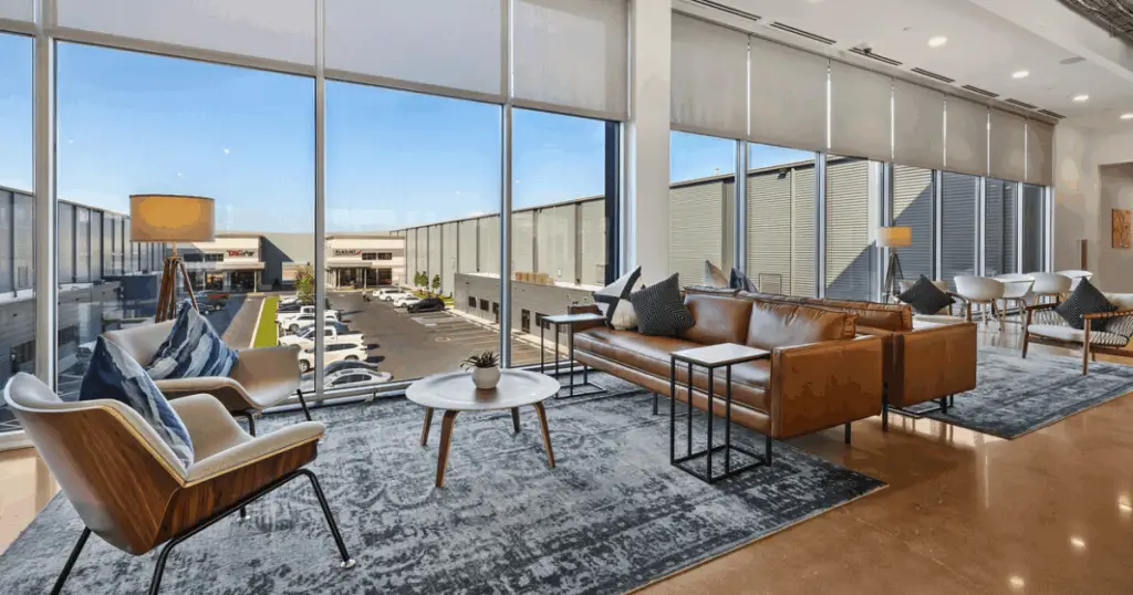 Shared coworking lounge at Venture X Braniff Centre in Dallas, Texas, featuring modern seating, large windows, and views of the surrounding business park.