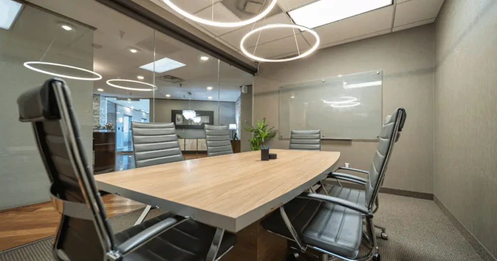 Modern meeting room at Strive Coworking Workspaces featuring a wood conference table, ergonomic chairs, glass walls, whiteboard, and contemporary ring lighting.