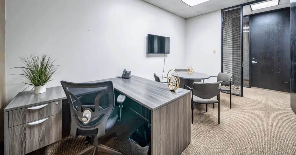 Furnished private office in North Dallas at Strive Workspaces with executive desk, guest seating, and wall-mounted display.