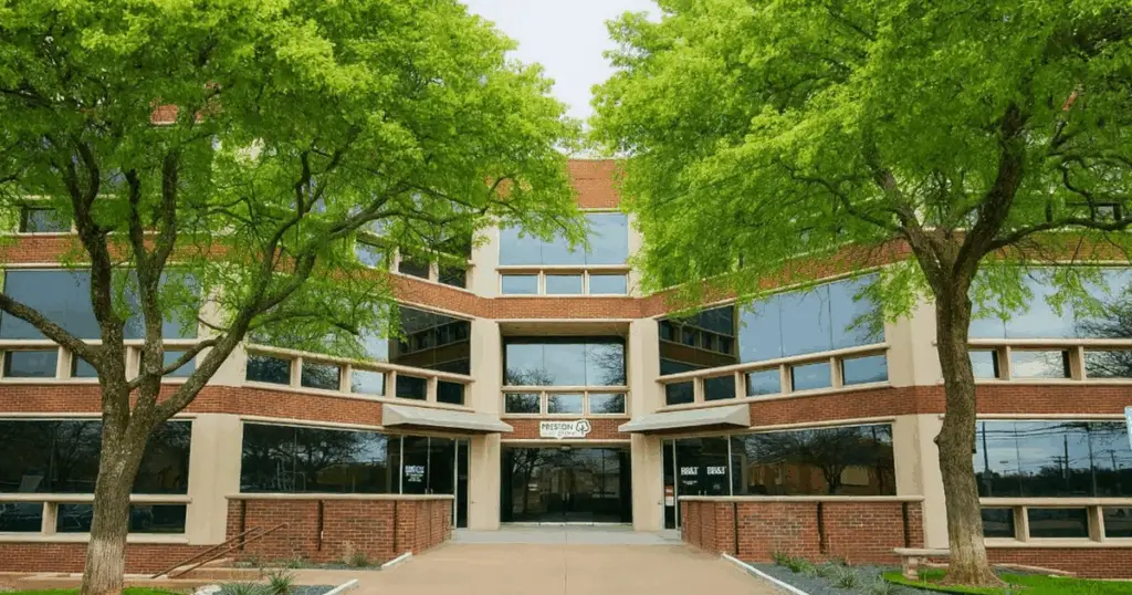 Exterior front entrance of Strive Coworking Workspaces North Dallas, a modern office building surrounded by trees.