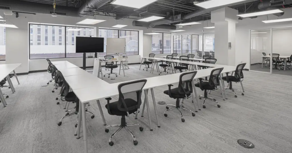 Large training room at Strive Coworking Workspaces with U-shaped tables, rolling chairs, and AV display.