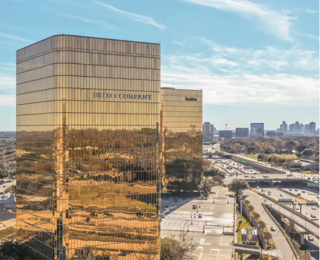 Exterior view of Flex at The Gild in Dallas, Texas, featuring a reflective glass office tower with views of nearby highways and the Dallas skyline.