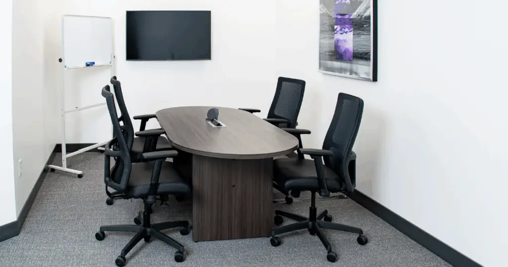 Small meeting room at Strive Coworking Workspaces with an oval conference table, ergonomic chairs, wall-mounted display, and whiteboard.