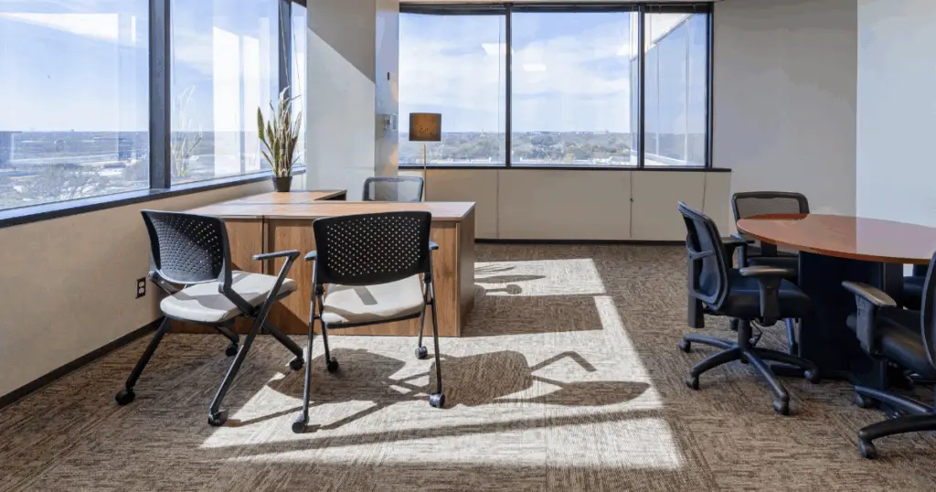 Private office at Strive Coworking Workspaces with multiple workstations, meeting table seating, and large windows providing natural light.