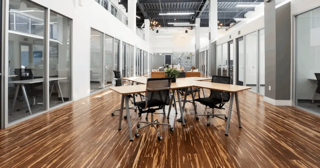 Open hot desk workspace at Strive Coworking Workspaces with shared tables, ergonomic seating, and private offices along a bright central corridor.