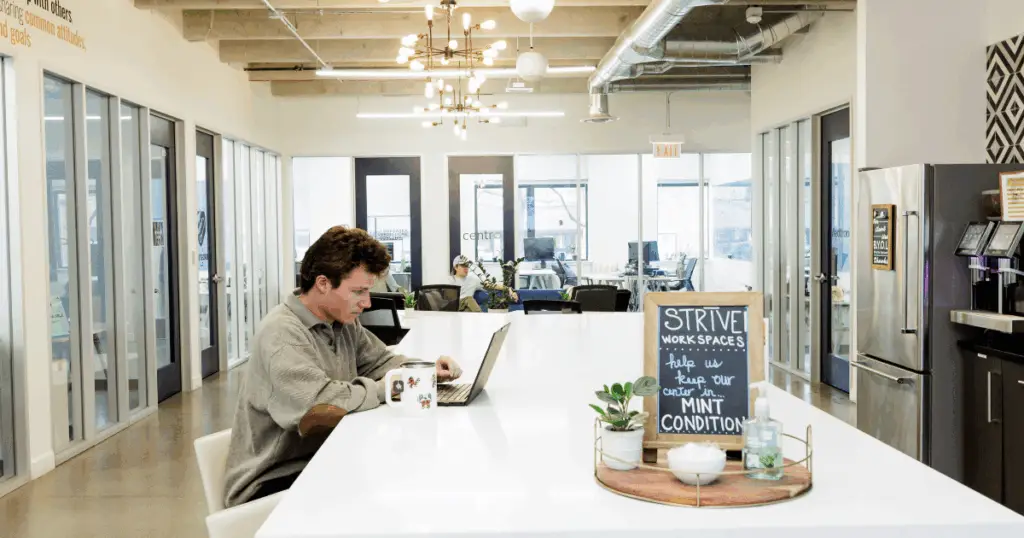Person working on a laptop at a shared coworking table inside a modern Strive Workspaces office.