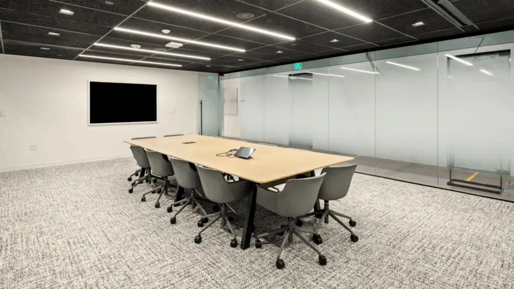 Glass-walled meeting room with conference table, rolling chairs, and AV display available to virtual office members at Strive Coworking Workspaces.
