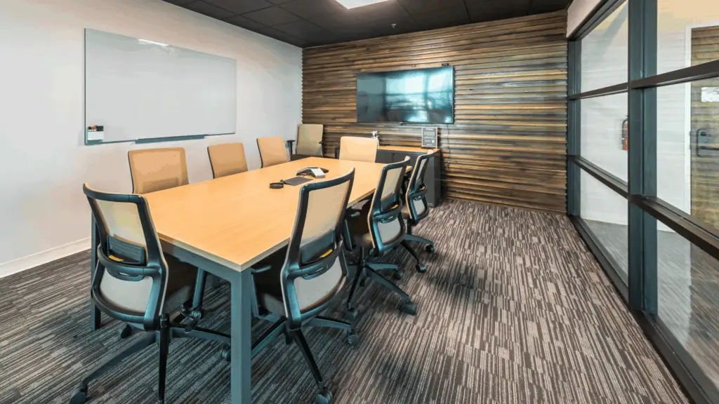 Glass-walled meeting room with conference table, whiteboard, and AV display available to virtual office members at Strive Coworking Workspaces.