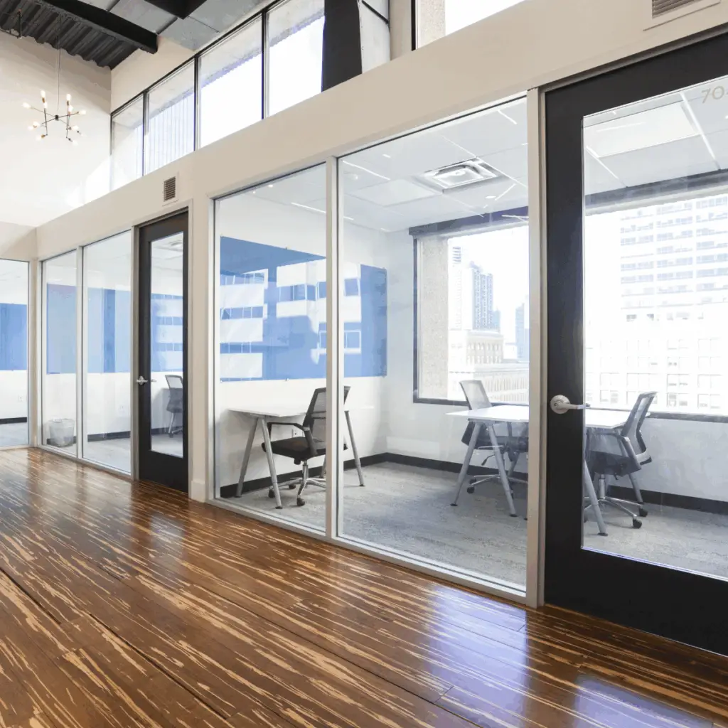 Glass-front private offices at Strive Coworking Workspaces with furnished desks and natural light along a modern corridor.
