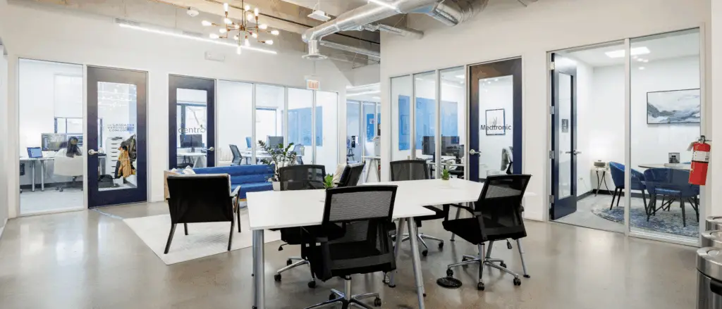 Open hot desk workspace at Strive Coworking Workspaces with shared tables, ergonomic seating, and glass-walled private offices.